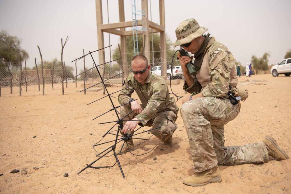 Two soldiers communicate with command via ground-based antenna communications.
