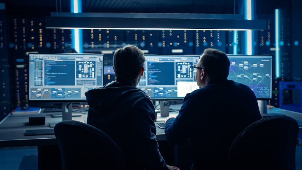 Two analysts compare data in a command center.