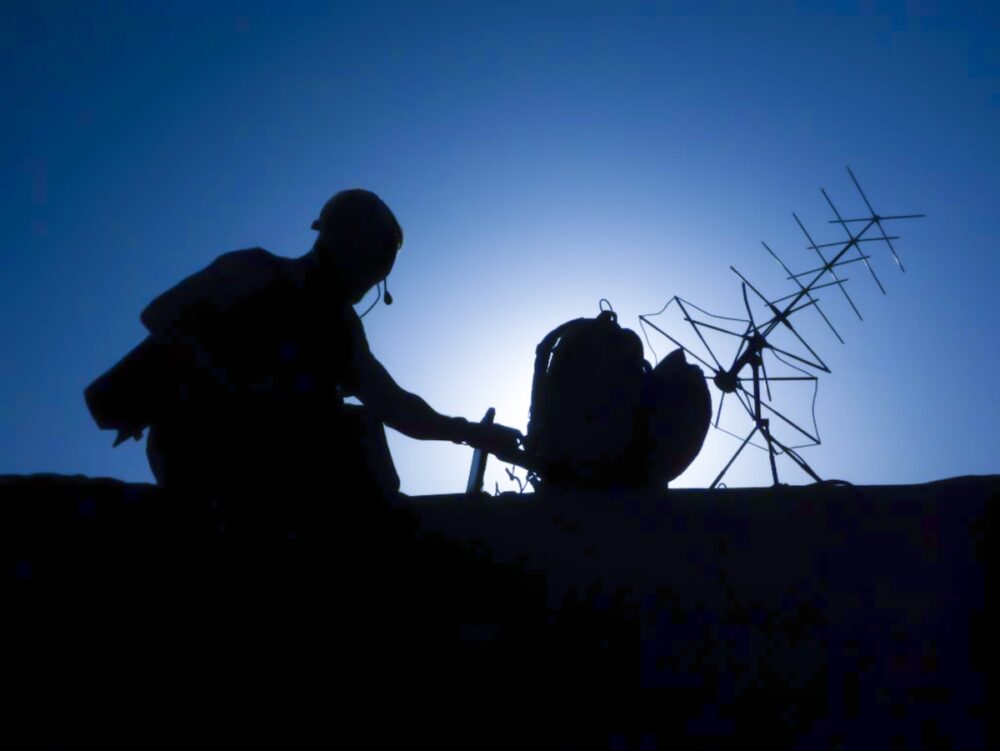 A soldier adjusts a ground-based antenna.