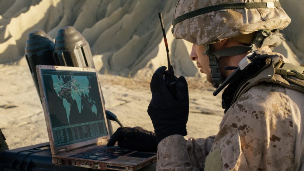 Ground-based soldier calls in coordinates via radio, views map on a laptop in the field.