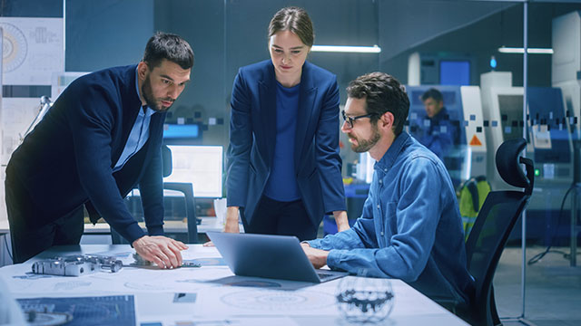 Diverse Team of Engineers, Managers Talking at Conference Table, Look at Blueprints